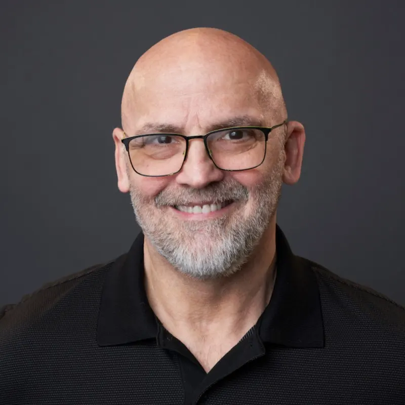 Marco Rigazio smiling, wearing glasses and a black collared shirt